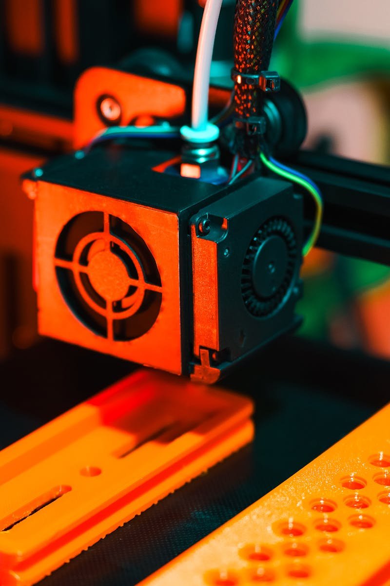 Detailed view of a 3D printer in action, extruding orange plastic components.